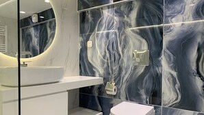 Un baño moderno con un lavamanos blanco, un inodoro y paredes con diseño de mármol.