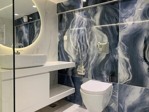 Une salle de bain moderne avec un lavabo blanc, des toilettes et des murs à motifs de marbre.