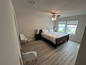 Ein Schlafzimmer mit einem Bett, einem Deckenventilator, einem Fenster mit Jalousien und einem Sessel.