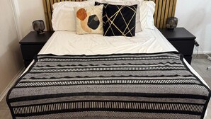 Een keurig opgemaakt slaapkamer met een bed, nachtkastjes, een houten hoofdbord, een klok en een ingelijst kunstwerk aan de muur.