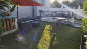 Een terras met tuinmeubilair, een rode parasol en een kleine waterpartij.