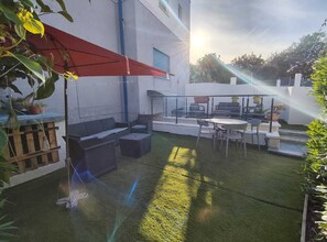 Eine Terrassenfläche mit Gartenmöbeln, einem roten Sonnenschirm und einem kleinen Wasserspiel.
