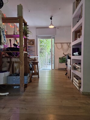Une pièce avec un plancher en bois, un bureau avec une chaise, un luminaire suspendu et une porte donnant sur l’extérieur.