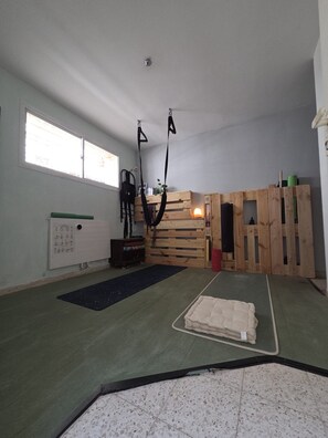 Una habitación con un tapete de yoga, una cama pequeña, un muro de madera y una ventana.