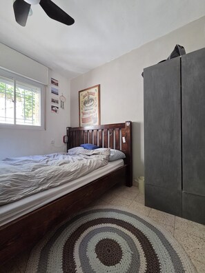 Une chambre à coucher avec un lit, un ventilateur de plafond, une fenêtre, une affiche et une armoire.