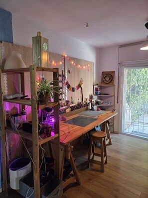 Un taller con una larga mesa, taburetes, estanterías y una ventana con vistas.