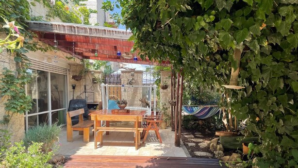 Eine Holzterrasse mit Tisch und Stühlen, umgeben von Grünpflanzen und einer Hängeampel.