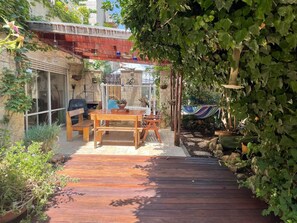 Una terraza de madera con una mesa y sillas, rodeada de vegetación y un jardín colgante.