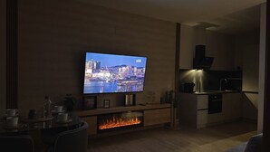A modern living room with a flat-screen TV, a dining area, and a kitchen. - Flower Beach Helgueras 1 - 6091 (Noja)