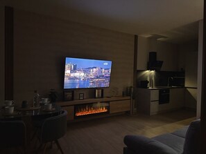 Ett modernt vardagsrum med en platt-TV, en matplats och ett kök.
