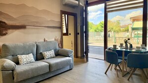 A modern living room with a sofa, a dining table with chairs, and a large window with a view of the outdoors. - Flower Beach Helgueras 1 - 6091 (Noja)