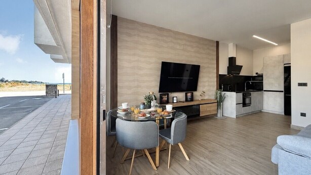A modern interior with a dining area, kitchen, and a large TV. - Flower Beach Helgueras 1 - 6091 (Noja)
