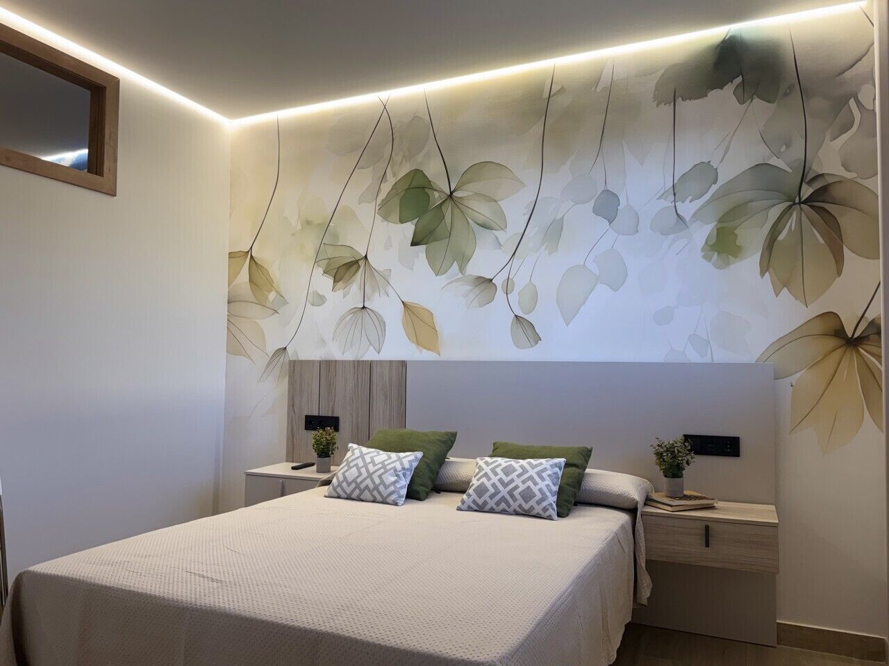 Une chambre moderne avec un grand lit, deux tables de chevet, une commode et un mur orné de motifs végétaux.