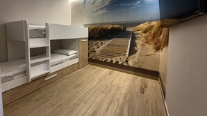 A room with bunk beds, a wooden floor, a beach-themed wall mural, and a ceiling light. - Flower Beach Helgueras 1 - 6091 (Noja)