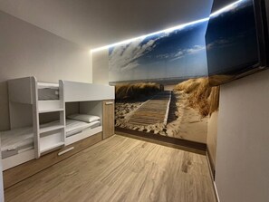 A room with bunk beds, a wooden floor, a beach-themed wall mural, and a ceiling light. - Flower Beach Helgueras 1 - 6091 (Noja)