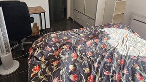 Un dormitorio con cama, escritorio, silla, armario y radiador.