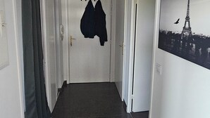 Un pasillo con suelo de baldosas, una puerta con un abrigo colgado y un cuadro en la pared con la Torre Eiffel.