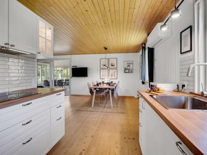 Eine moderne Küche mit Holzboden, weißen Schränken, einem Essbereich mit Tisch und Stühlen und einem großen Fenster.