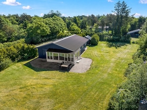 Ein Haus mit großem Wintergarten, einer gepflasterten Terrasse und einem gepflegten Rasen.
