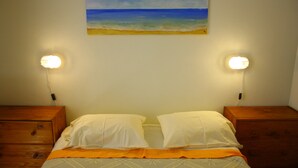 Un lit avec des oreillers blancs, une couvre-lit orange et un tableau représentant une plage accroché au mur.
