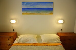 A bed with white pillows, an orange bedspread, and a painting of a beach on the wall. - Rustic house featuring traditional Portuguese handicrafts (Nazaré)