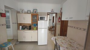 A compact kitchen with white cabinets, a microwave, a refrigerator, and a small dining table with a patterned tablecloth. - Rustic house featuring traditional Portuguese handicrafts (Nazaré)
