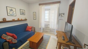 A living room with a blue sofa, a wooden coffee table, a TV on a stand, and a window with curtains. - Rustic house featuring traditional Portuguese handicrafts (Nazaré)
