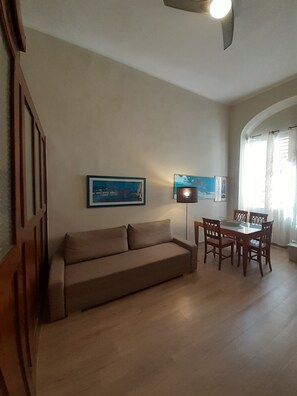 Ein Wohnzimmer mit einer Couch, einem Esstisch, Stühlen und zwei Wandleuchten.