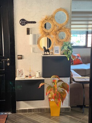 Een moderne woonkamer met een zwarte deur, een aan de muur bevestigde gitaar, drie ronde spiegels, een bord met daarop 'Welkom', een klein beeldje, een QR-code en een potplant.