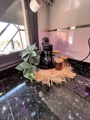 Een koffieapparaat, een plant en een klein houten krukje op een marmeren aanrecht.