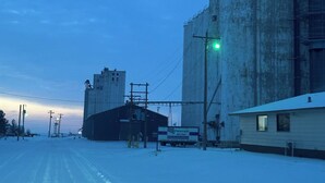 Een besneeuwd industriegebied met grote graansilo's, een vrachtwagen en een klein gebouw.