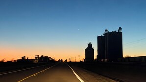 Een snelweg met een heldere lucht, verre gebouwen en een zichtbare maan.
