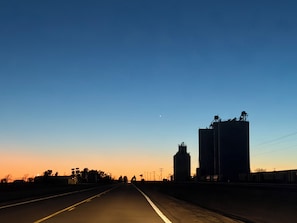 Carretera con cielo despejado, edificios lejanos y luna visible.
