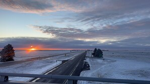 Een snelweg met sneeuwbedekte velden en een ondergaande zon in de verte.