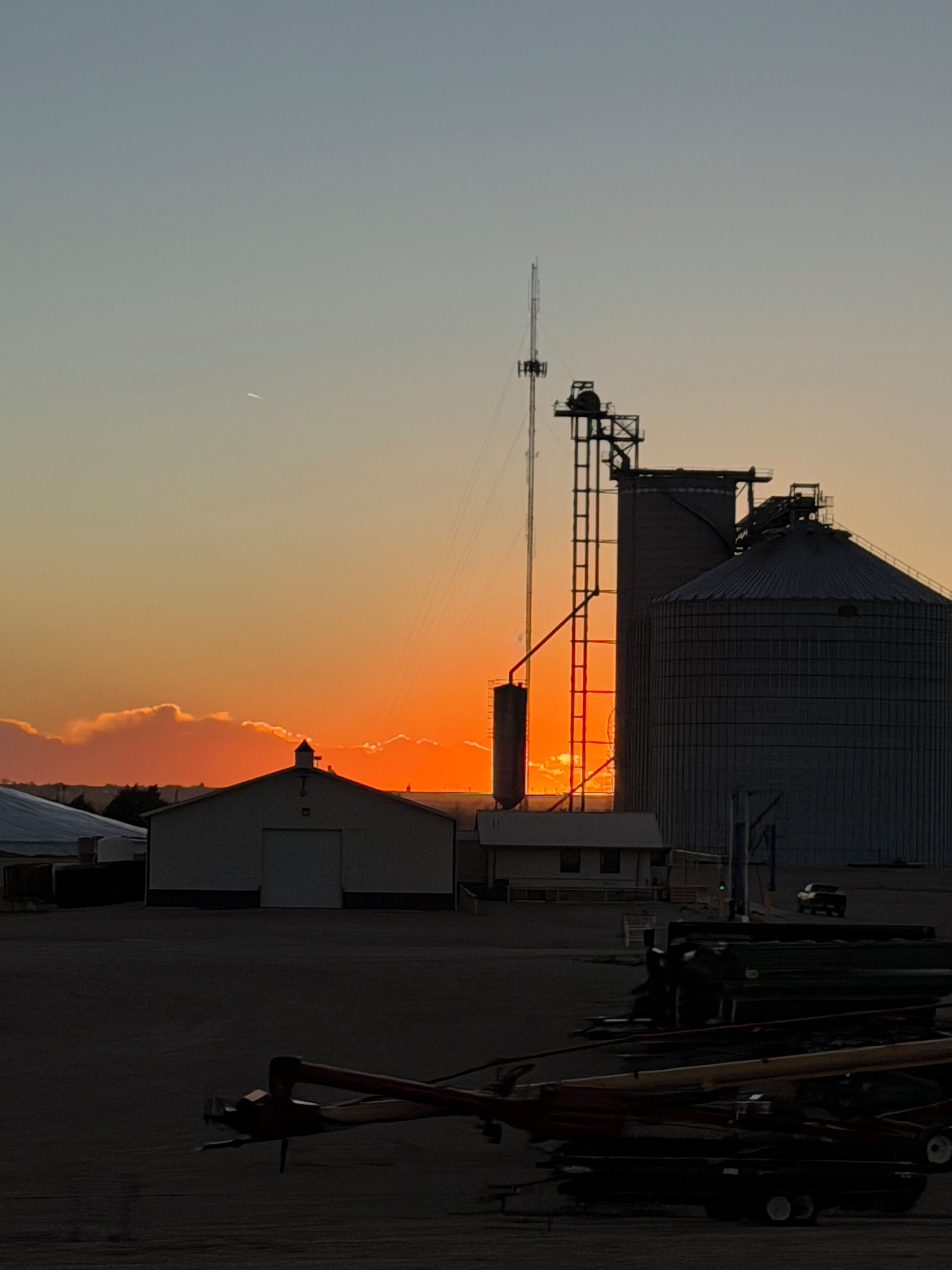 A grain silo and a building with a flat roof, both silhouetted against a sunset sky.