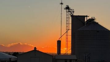 A grain silo and a building with a flat roof, both silhouetted against a sunset sky.