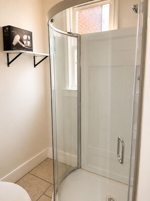 Een douchehoek met glazen deur, een wit toilet en een plank met een haardroger.
