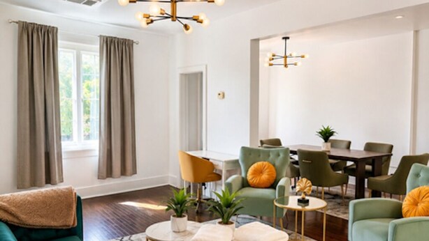 A modern living room with a green sofa, a round coffee table, and a dining area with green chairs.