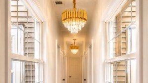 A hallway with a chandelier, white walls, and a wooden floor.
