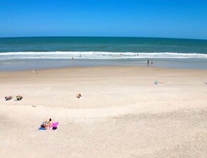 A beach with people sunbathing and swimming, and a clear blue sky. - Salt Life Suite - Oceanview + Pool + Walkable to Entertainment (Jacksonville Beach)
