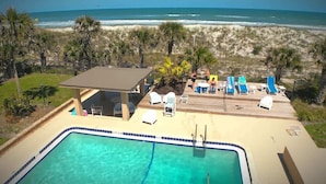 Une piscine à l’eau claire, une terrasse en bois, des chaises longues et une vue sur la plage et l’océan.