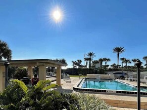 A clear blue sky, a swimming pool, palm trees, and a covered seating area. - Salt Life Suite - Oceanview + Pool + Walkable to Entertainment (Jacksonville Beach)