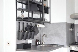 Een keuken met een modern design, voorzien van een roestvrijstalen spoelbak, een inbouwoven en een zwarte houder voor keukengerei met diverse keukentools.