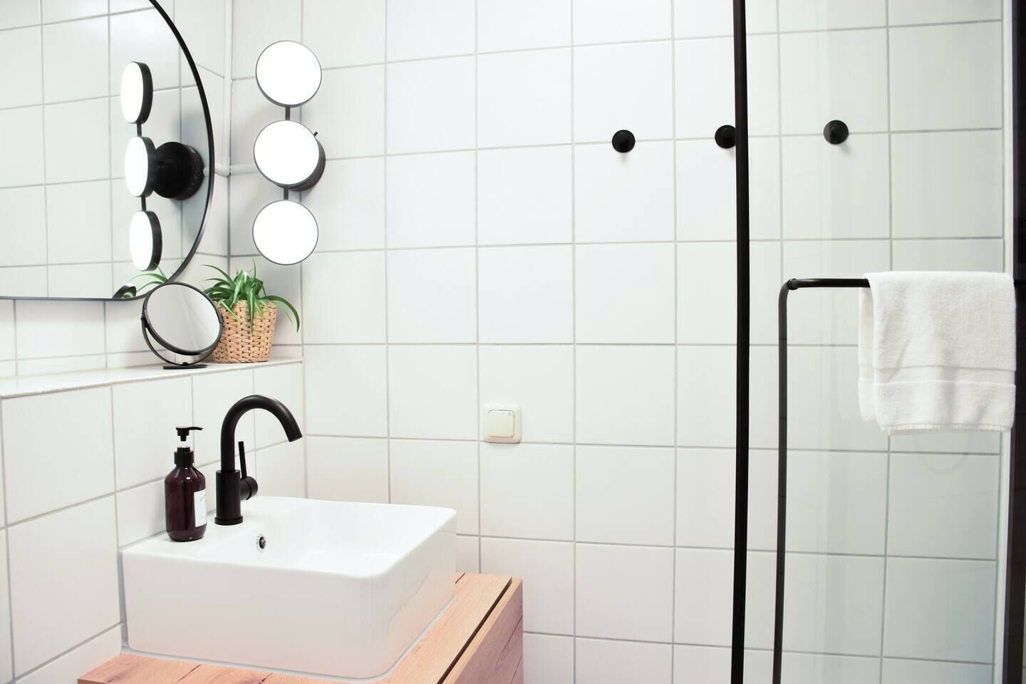Een moderne badkamer met een witte wastafel, een zwarte kraan en een spiegel met verlichting. Er is een douchegedeelte met een glazen deur en een handdoek op een rek.