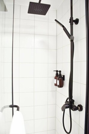 Una doccia con soffione a mano, rubinetto a parete e due flaconi di shampoo.