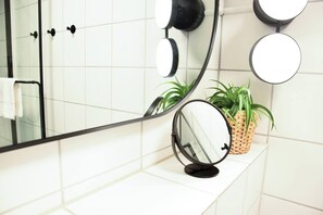 Een badkamer met een grote spiegel, twee kleinere spiegels, een handdoekhouder en een plant in pot.
