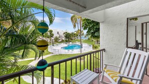 Ein Balkon mit weißem Stuhl, einem Pool und Palmen.