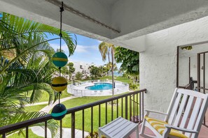 Ein Balkon mit weißem Stuhl, einem Pool und Palmen.