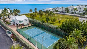 Ein Tennisplatz, umgeben von üppiger Vegetation mit Blick auf das Meer.