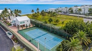 Ein Tennisplatz, umgeben von üppiger Vegetation mit Blick auf das Meer.